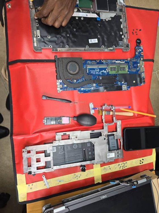 Un ingénieur Hankaka Technologies démonte un ordinateur portable professionnel sur un tapis antistatique de terrain rouge, dans les bureaux d'un client, le clavier, la carte mère, le dissipateur, la batterie et le stockage disposés dans l'ordre pour un remplacement de pièce sur site.