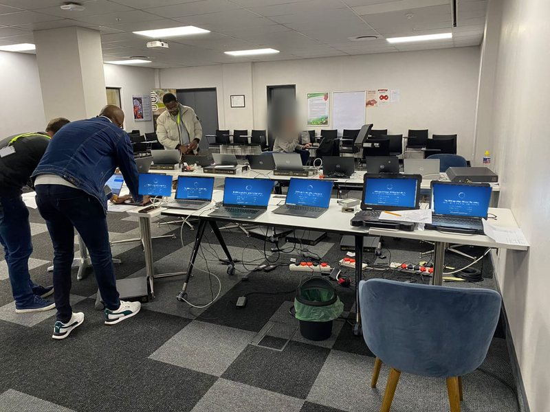 Hankaka Technologies engineers imaging and configuring a row of laptops on temporary staging tables during a client device refresh.